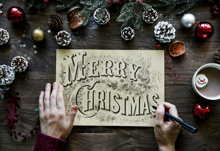 person writing Merry Christmas on paper in between Christmas decors